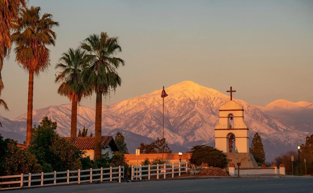 Redlands mission bell tower with palm trees and snow-covered mountains in the background at sunset.